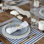 A wooden dining table with blue and white dinnerware and a blue and white striped coaster.