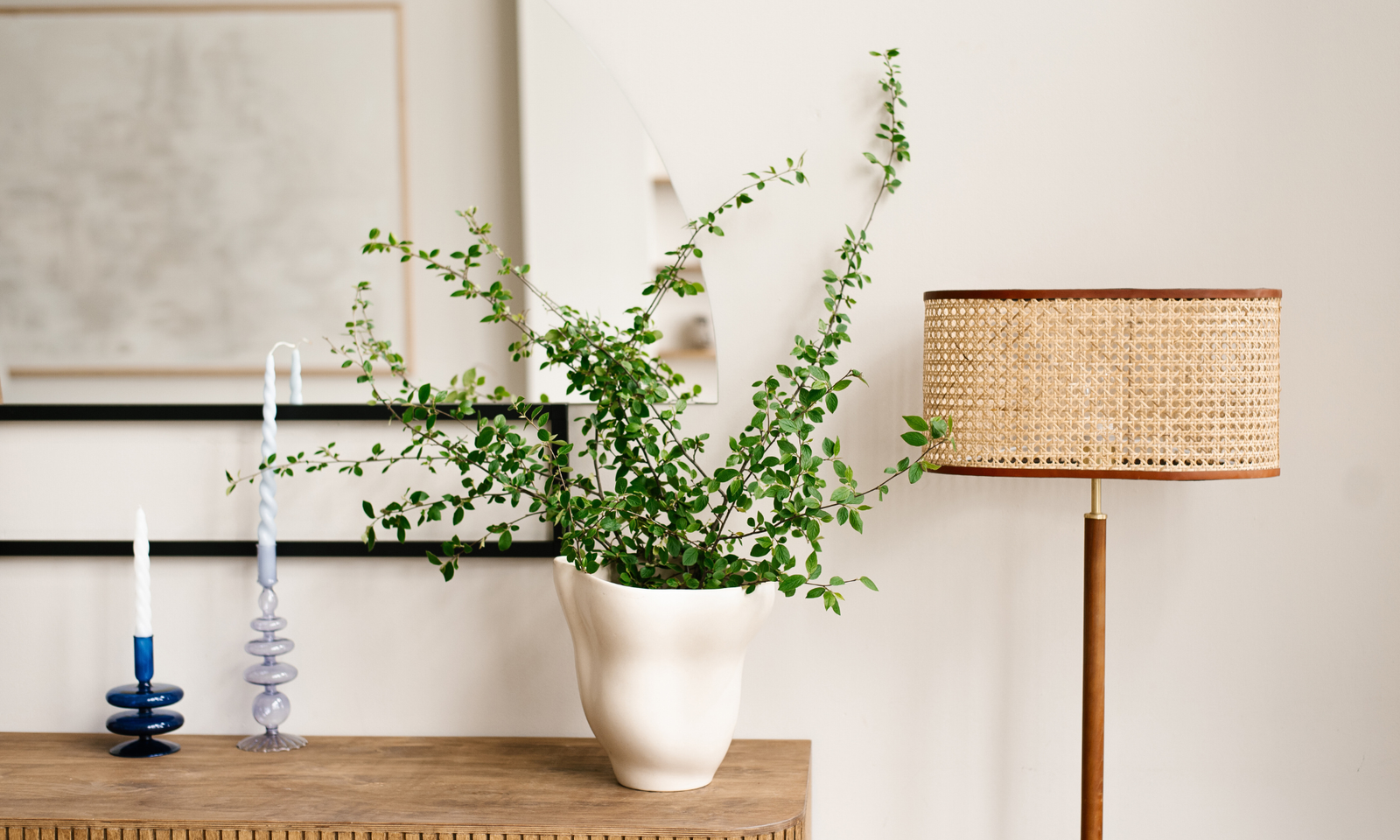 Indoor plants benefits with a plant on a wooden sideboard. Candle sticks and a floor lamp.