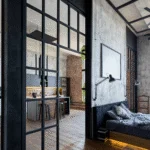 Industrial interior design with a kitchen in the background and a glass door from the bedroom with a black bed.