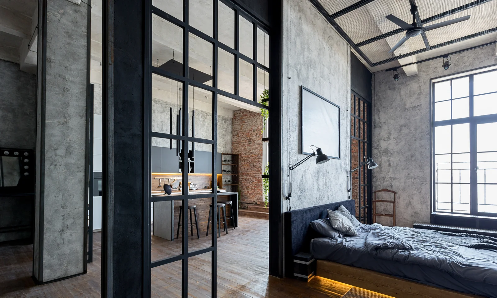 Industrial interior design with a kitchen in the background and a glass door from the bedroom with a black bed.