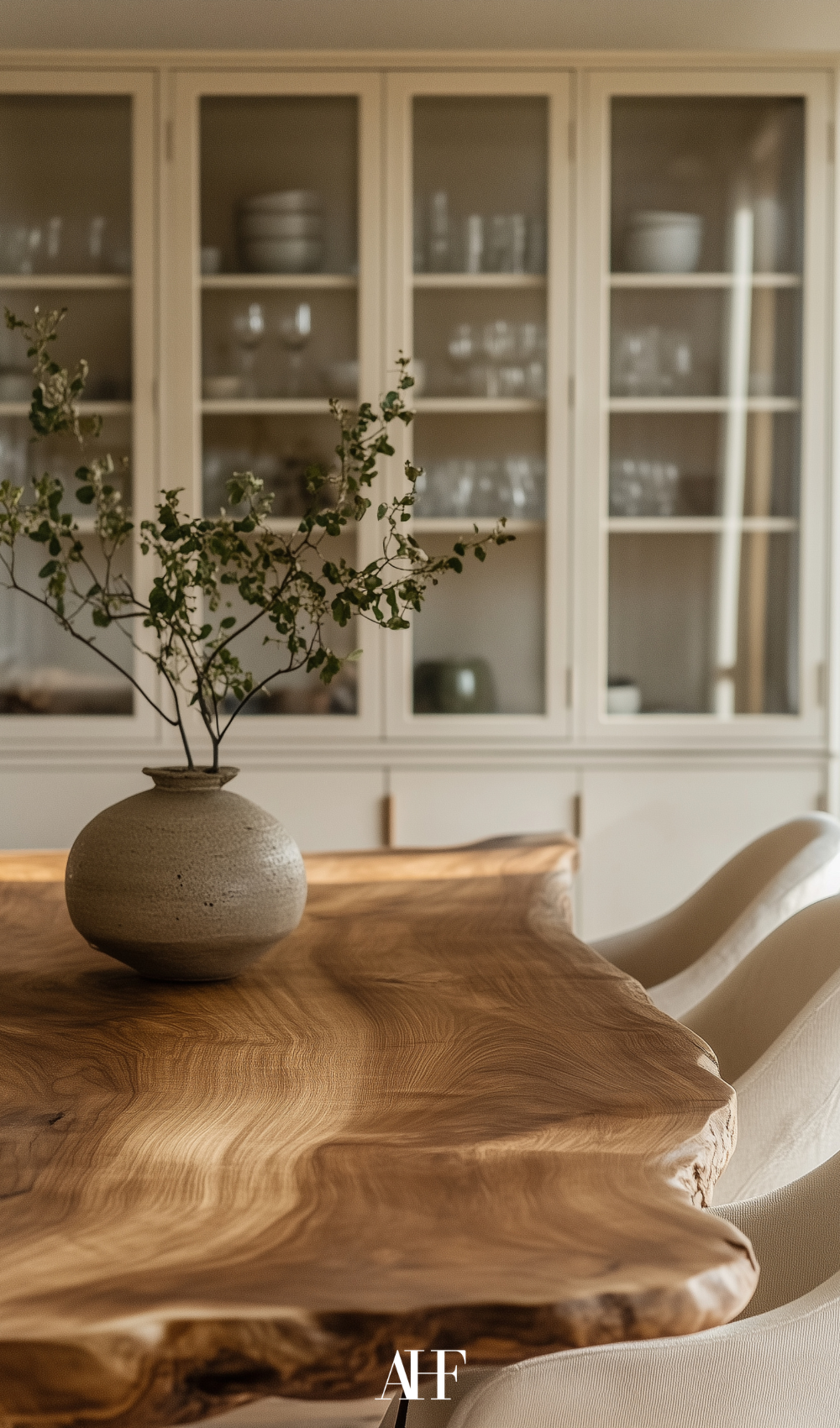 How to decorate your home - a wooden dining table with beige chairs, a large flower on the table. A glass cabinet in the backgroudn. 