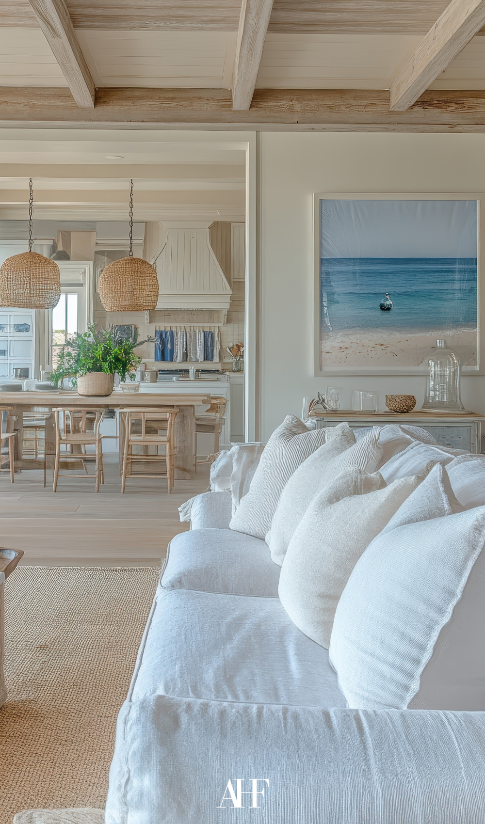 A beautiful coastal living room with a white couch, a blue wall art and a wooden dining table.