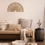 How to decorate your home. A rattan bench with lots of pillows on it. A vase next to the bench and a wooden latter against the wall.