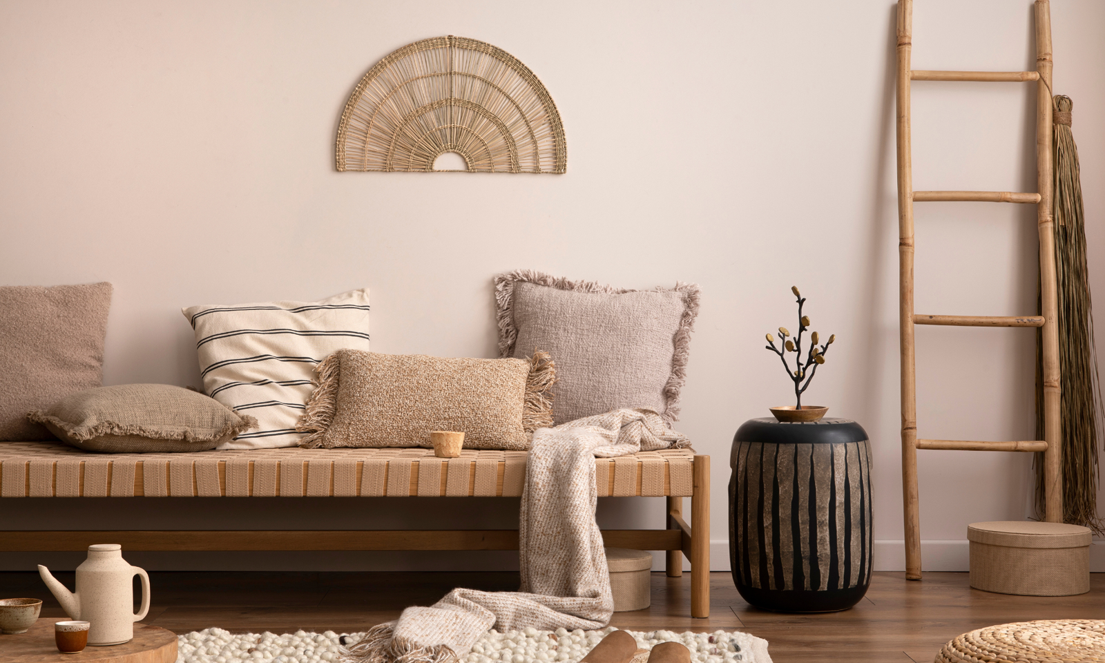 How to decorate your home. A rattan bench with lots of pillows on it. A vase next to the bench and a wooden latter against the wall.