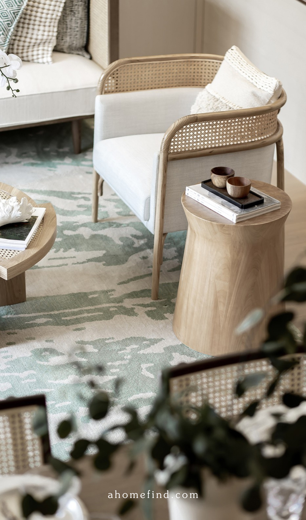 A scandinavian living room with a rattan armchair and white pillows. A green and white rug and some plants. 