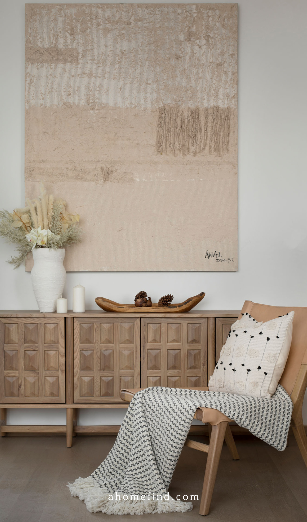 A beautifully styled armchair with a wooden sidetable and a large artwork on the wall. 