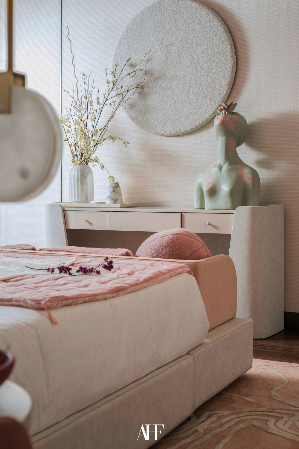 A bedroom color scheme with blush pink and warm grey. A closeup with a bed and a side board against the wall. A sculpture of a person on the side board.