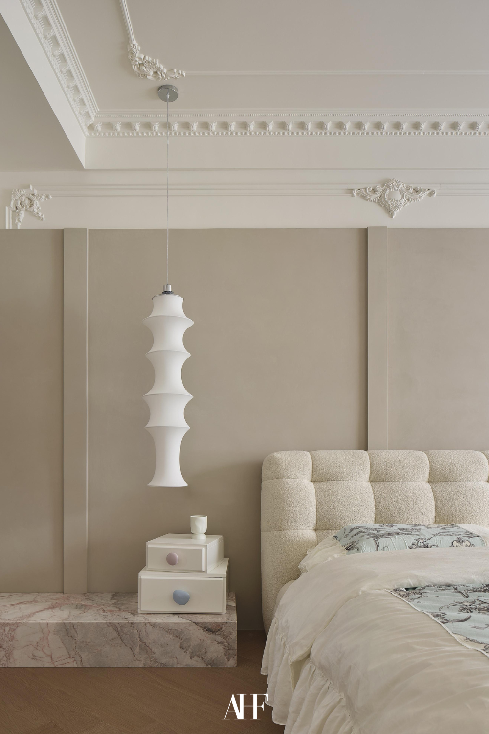 A neutral bedroom with a white bed, beige walls and a white bedside table. Details in the rooftop and white bedding with blue patterned details. 