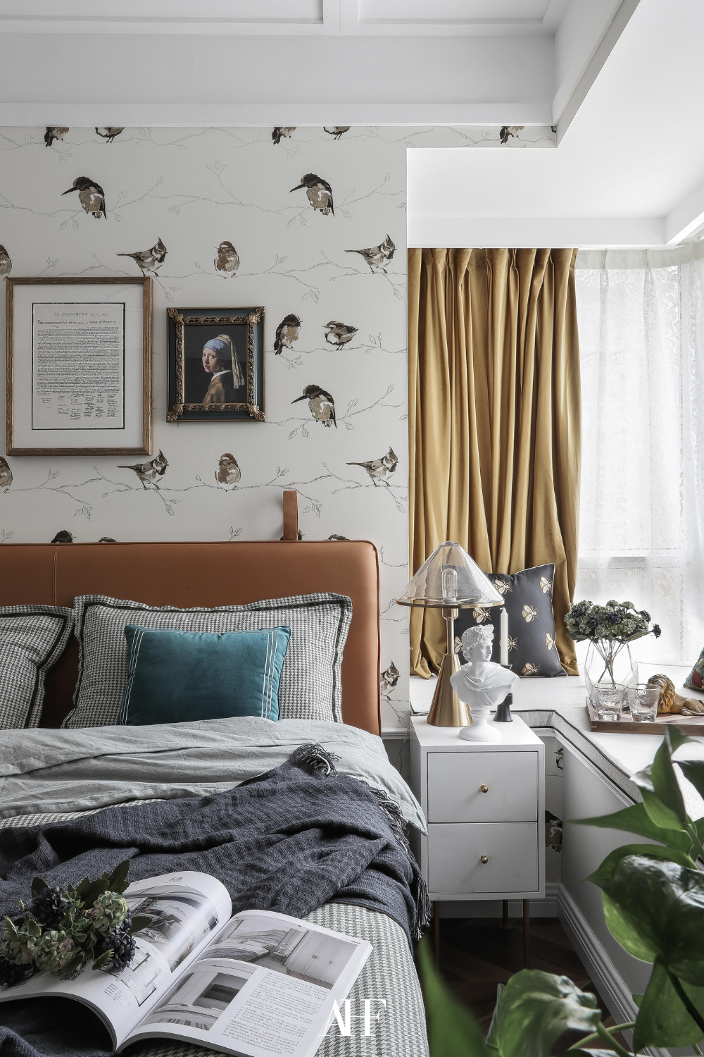 A deep teal and mustard colored bedroom with a bird tapet, a leather bed frame and a white bedside table. Lots of details.