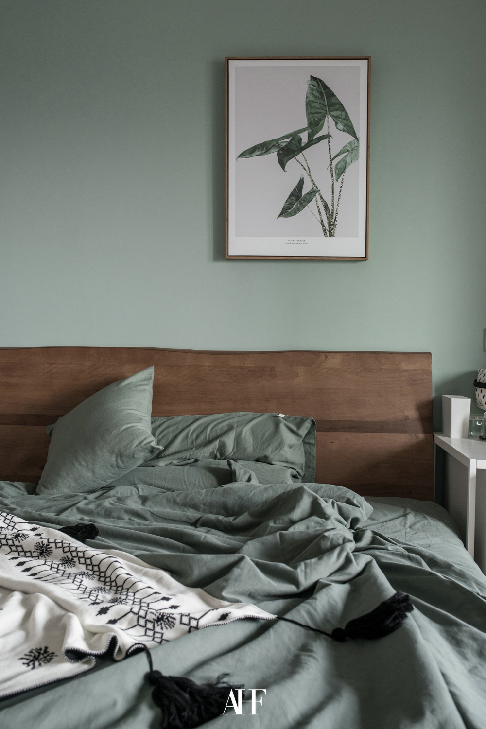 A sage green bedroom color combinations with a dark wooden bedframe, sage green bedding and a green wall with an artwork. 