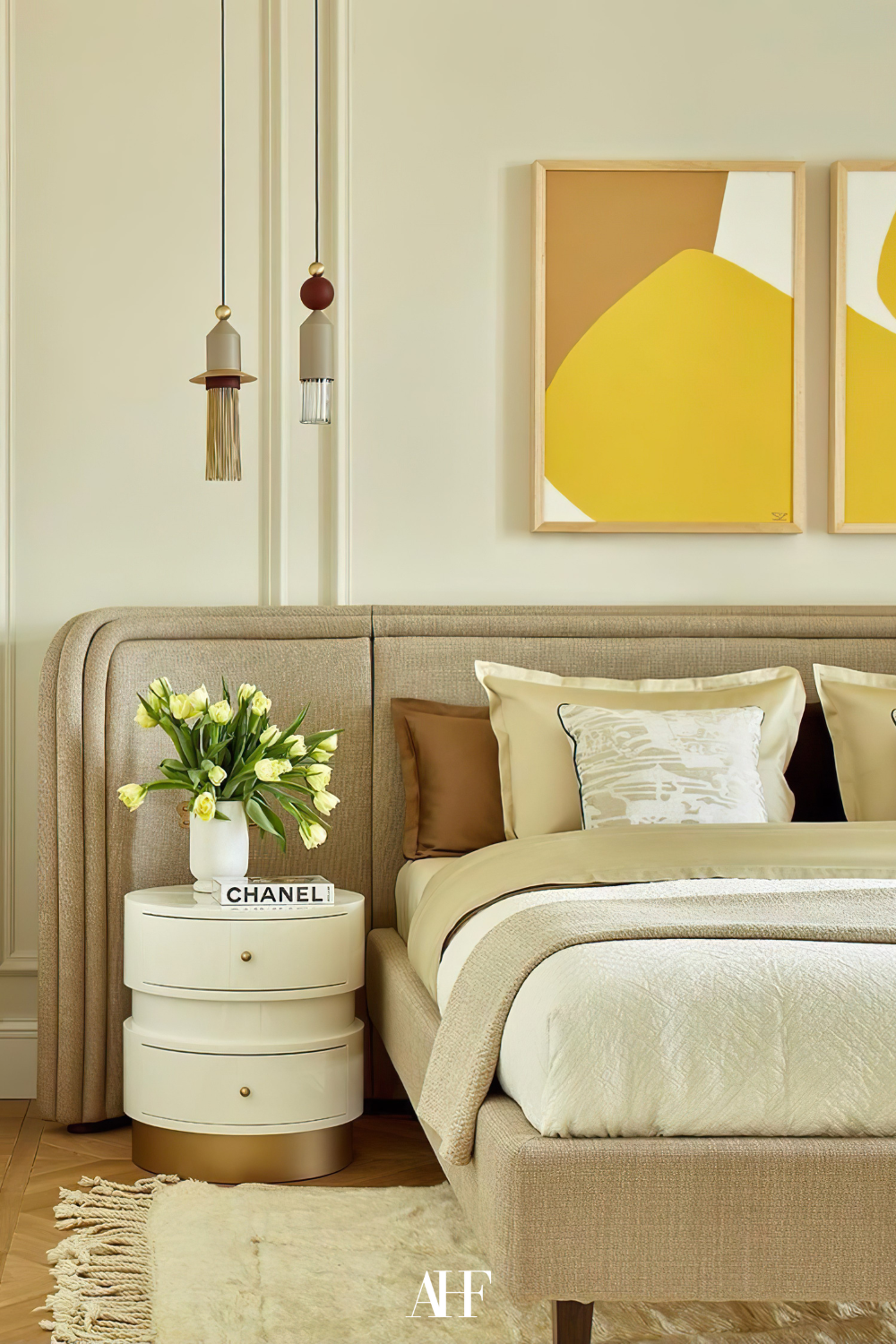 A modern bedroom with yellow details. Bedroom color combinations with white and beige. A bed in the middle with tucked in bedding, and a white bedside table with two lights hanging over it. 