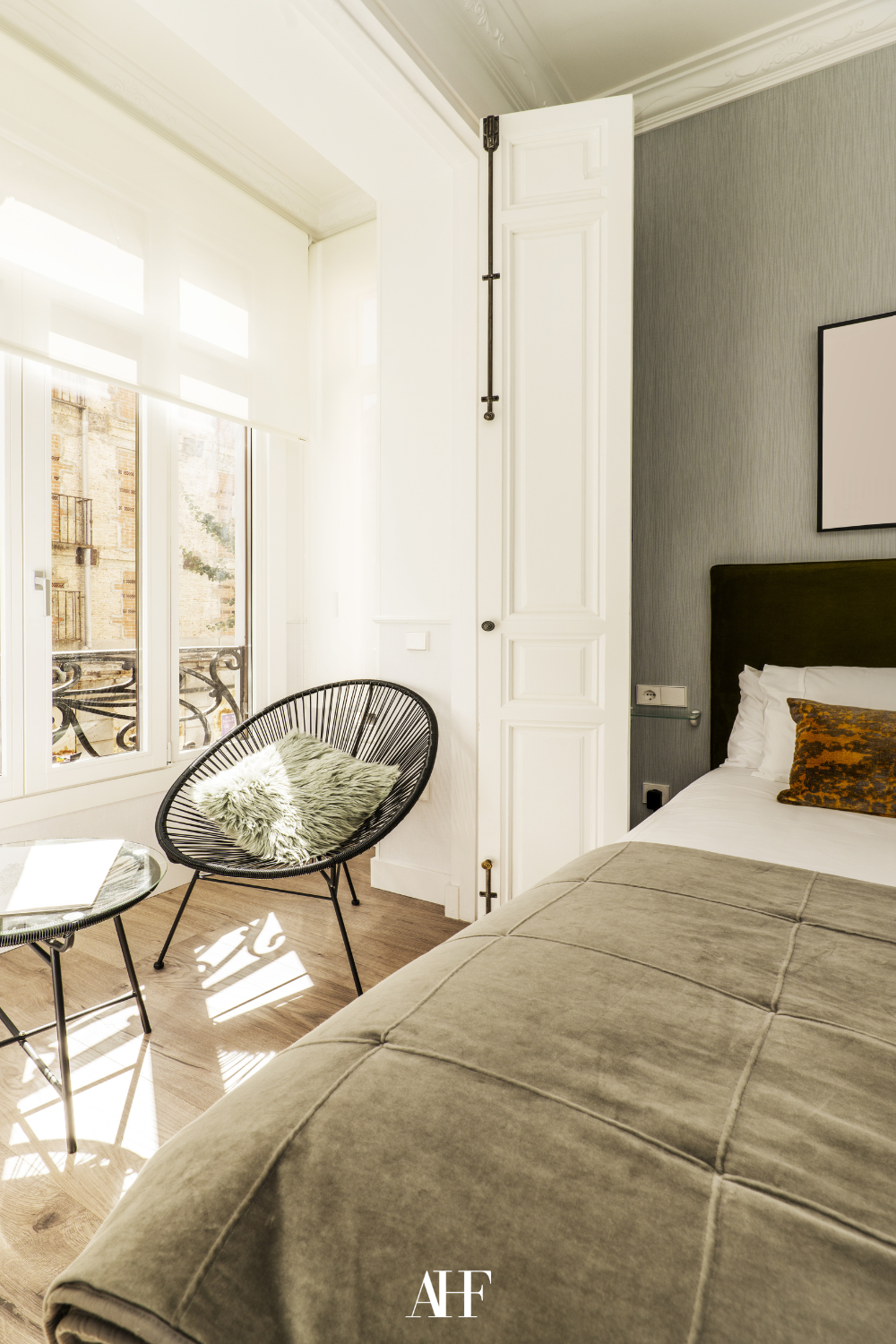 A beautiful bedroom with green details, large widows and a accent chair. 