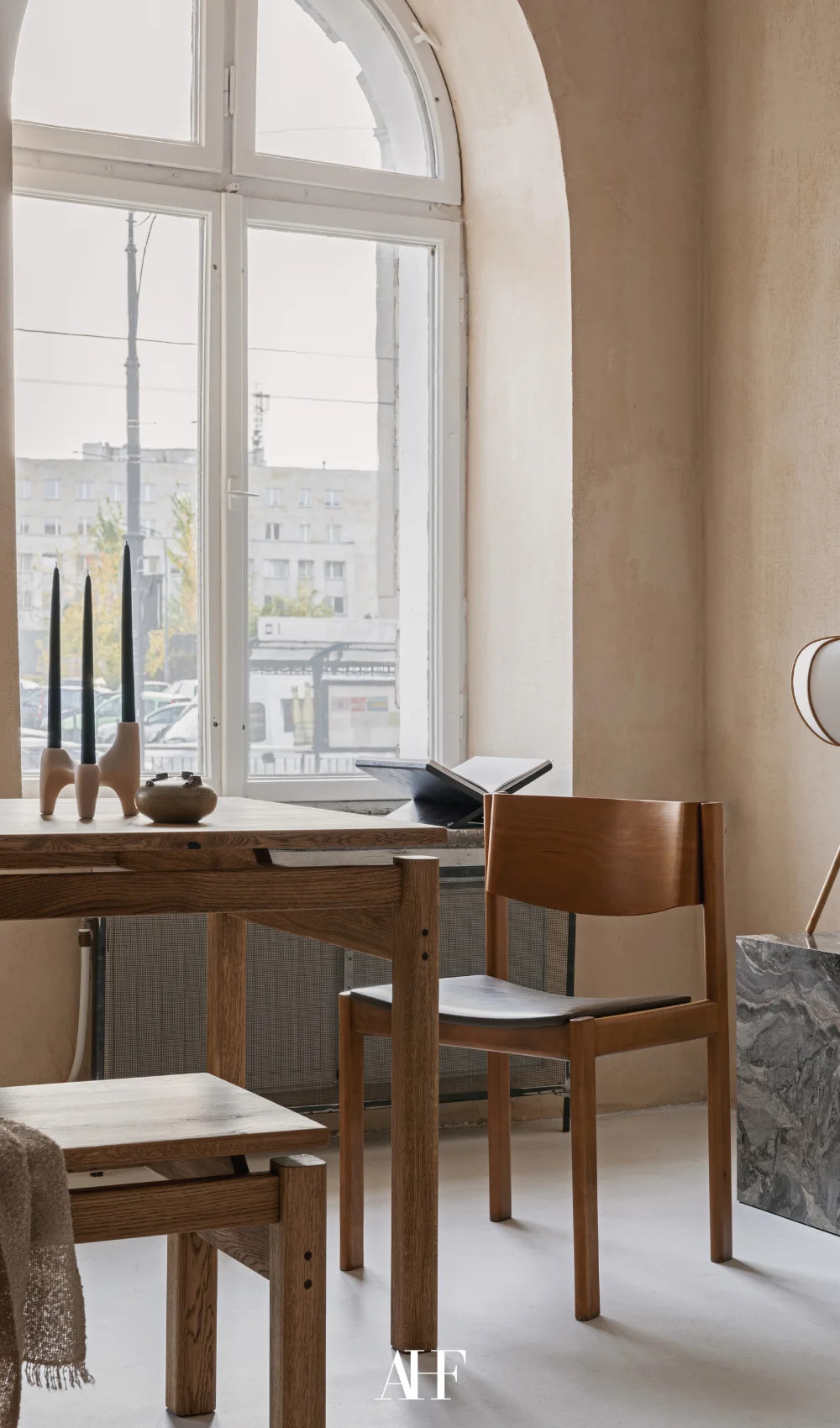 A dining room with wooden dining table and wooden dining chairs. A large curved window and some decorations on the table.