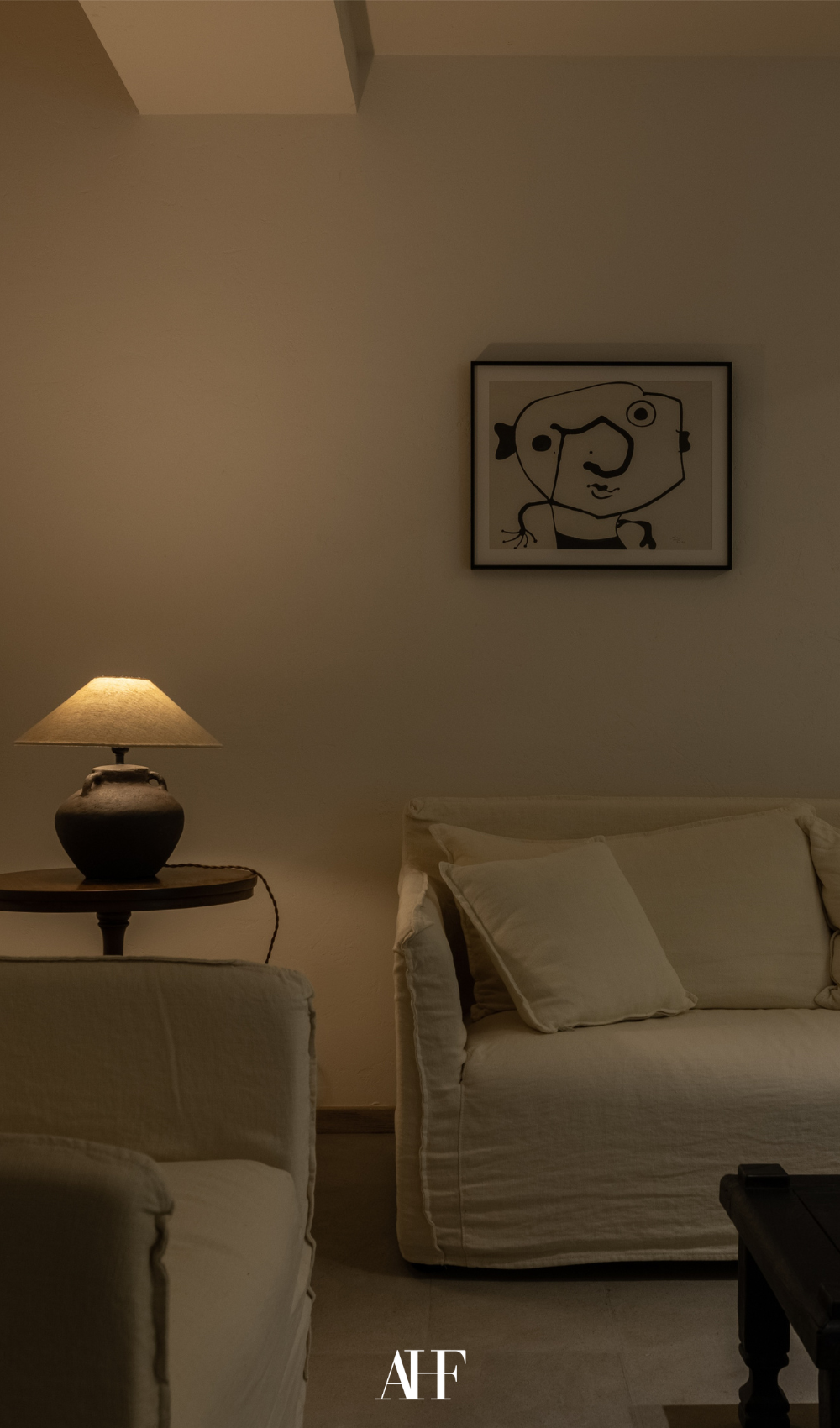A cozy living room with a cozy table lamp, two beige sofas and a wall art.