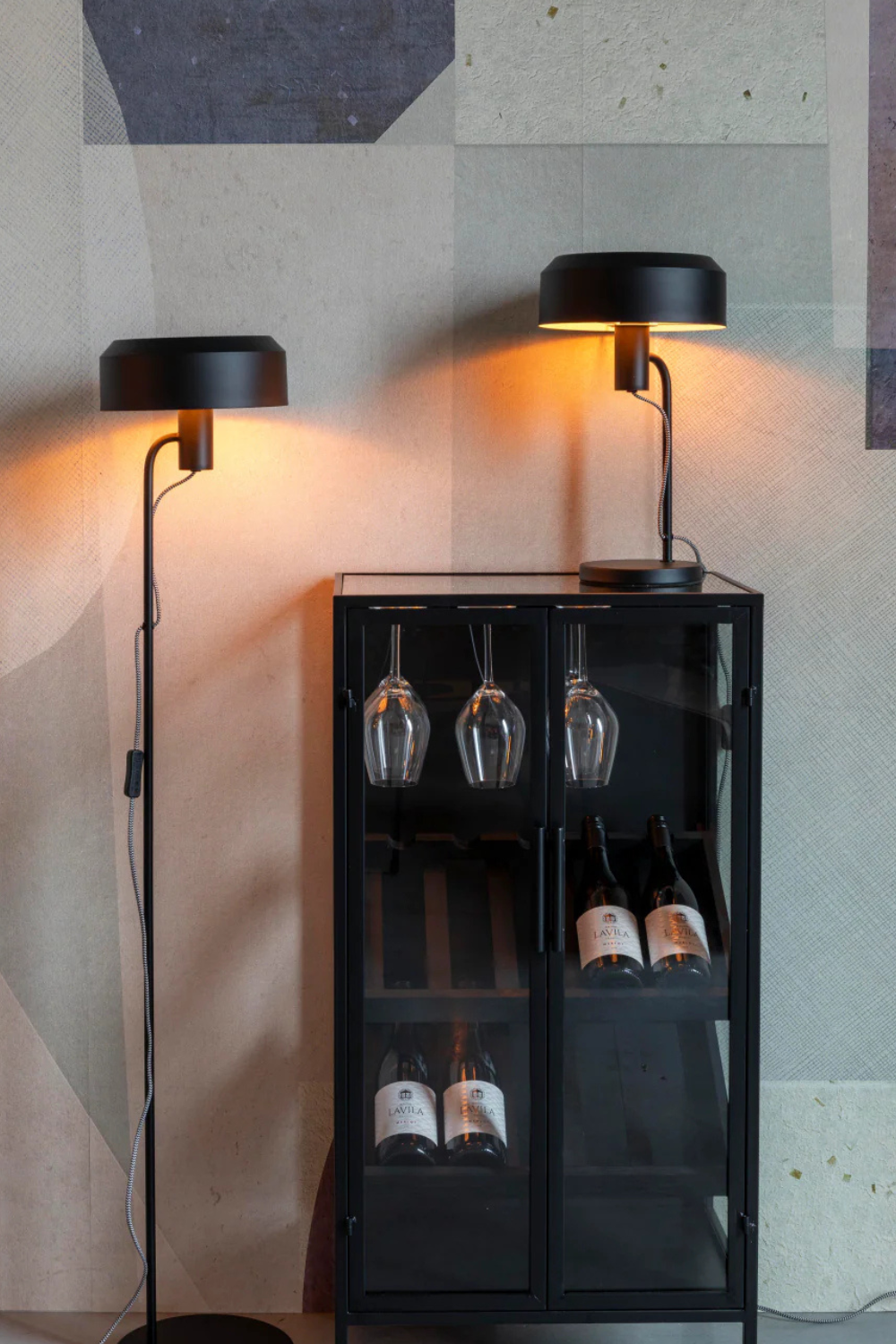 A matte black industrial table lamp on a black and glass side table. A matte black floor lamp next to the side table.
