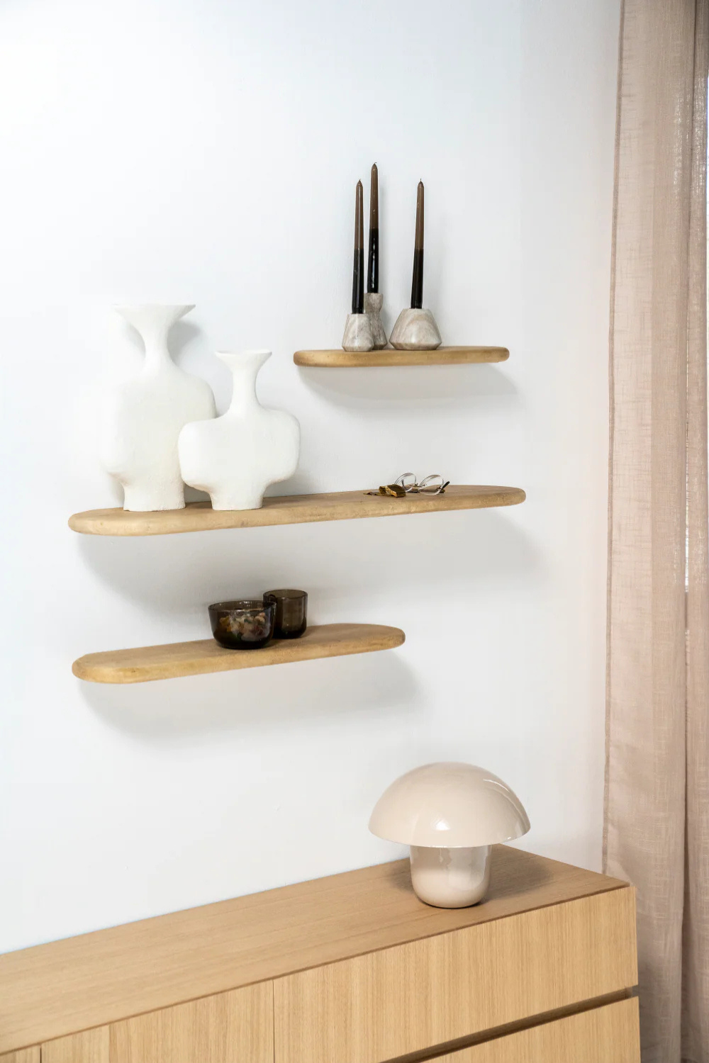 A mushroom lamp on a wooden bench with a white wall in the background, with wooden shelves.