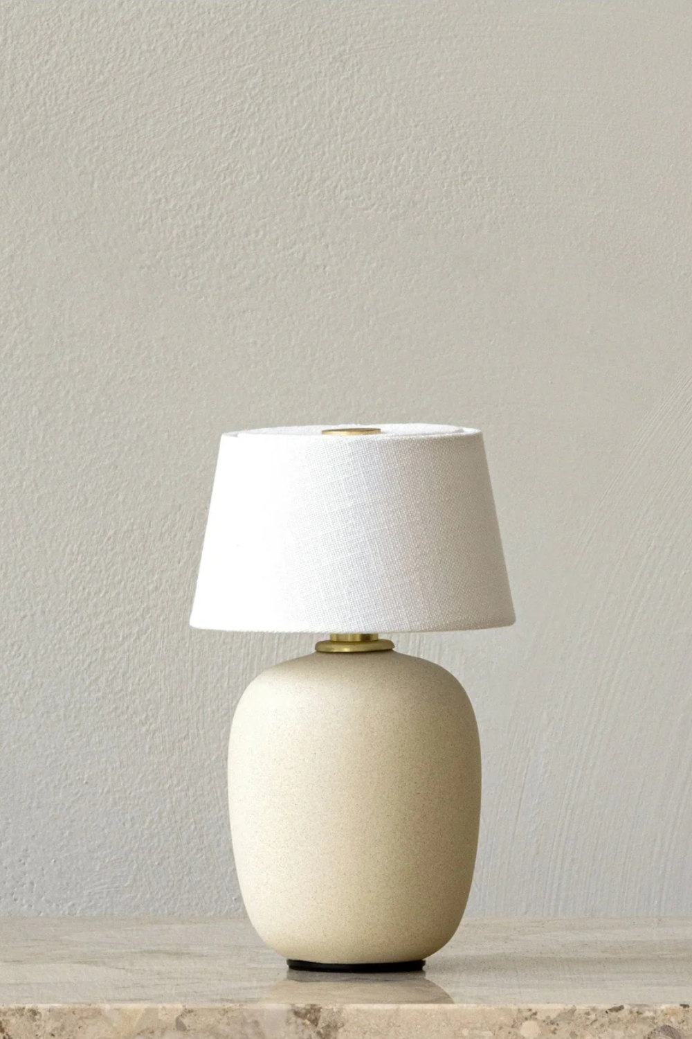 A dimmable table lamp in beige and white standing on top of a marble table with a white background. 