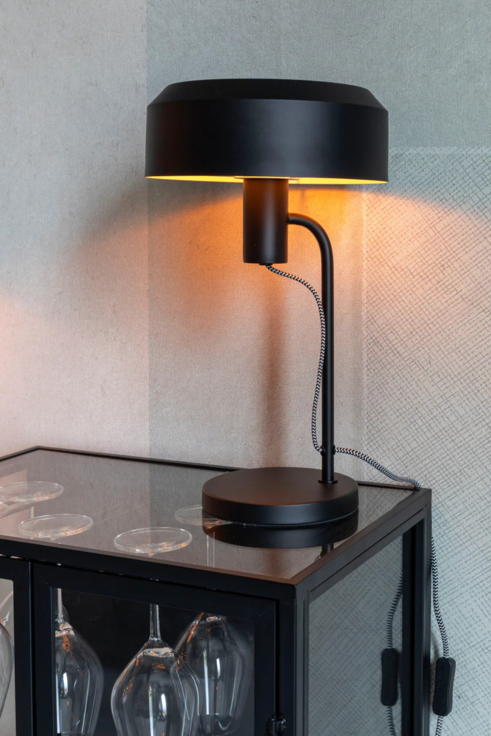 A matte black industrial table lamp on a black and glass side table.