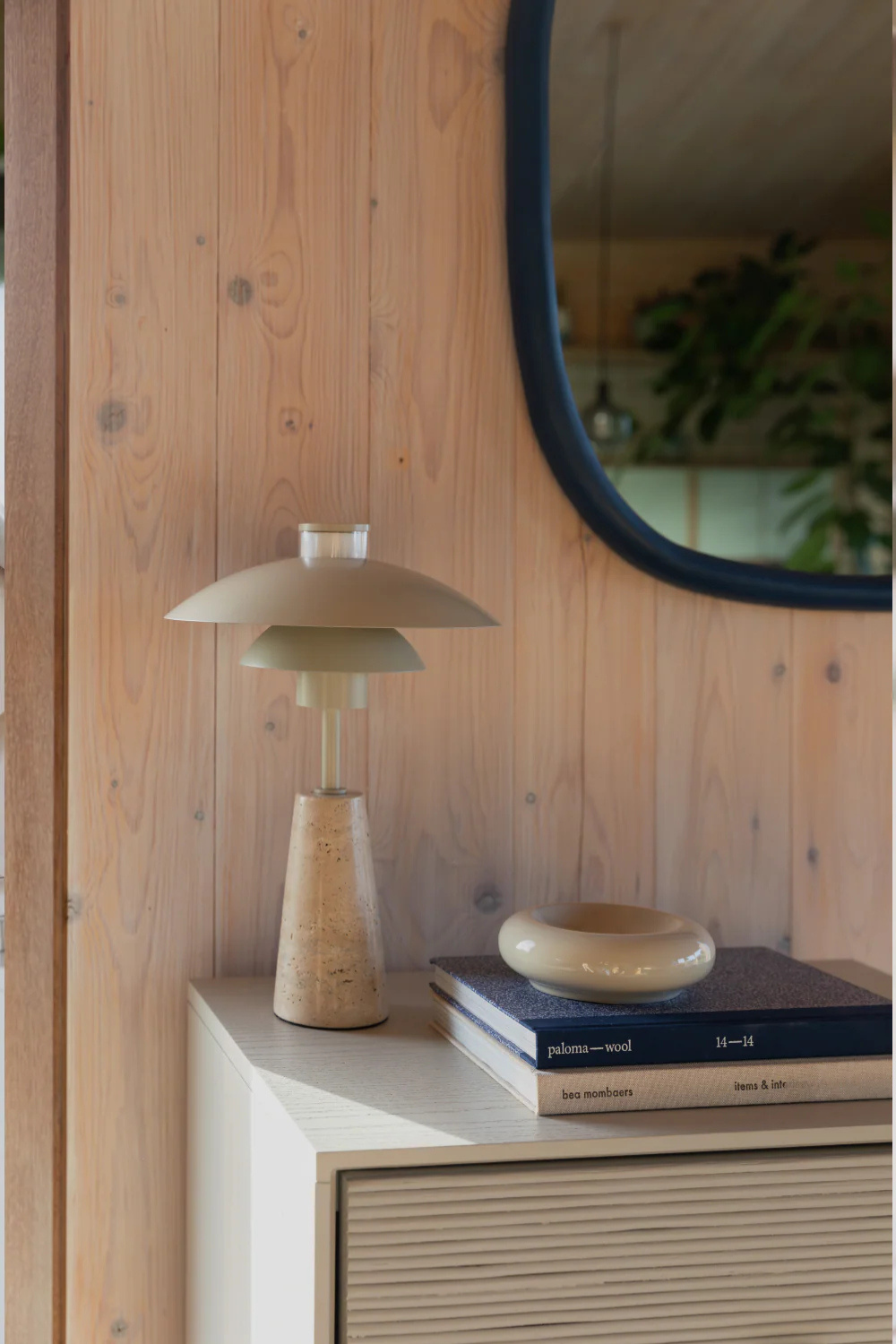 A modern neutral table lamp with a marble foot standing on a side board table with a mirror above. 