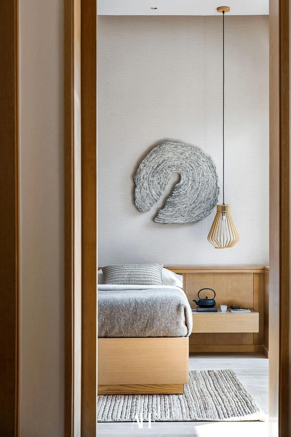 Japandi color palette bedroom with a wooden bedside table, neutral bedding and a large rug.