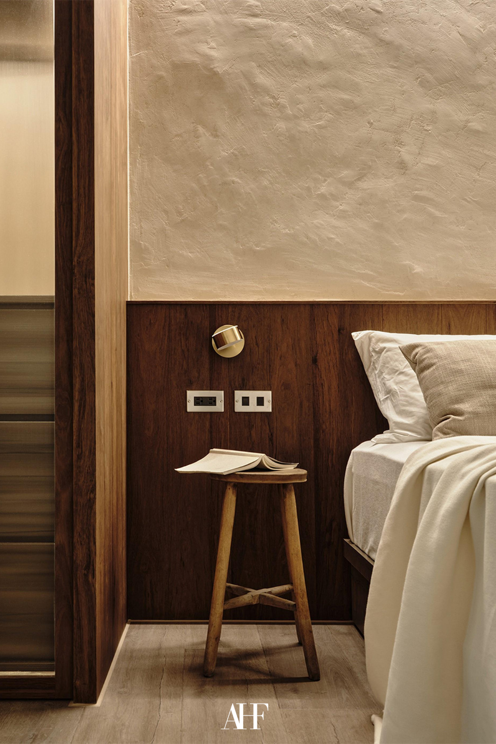 Cozy japandi bedroom ideas with dark wooden panel on the wall, white bedding in the bed and a wooden bedside table.