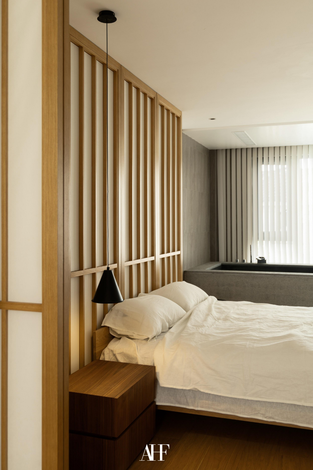 Japandi minimalist bedroom with wooden details on the wall, white bedding and a dark wooden bedside table.