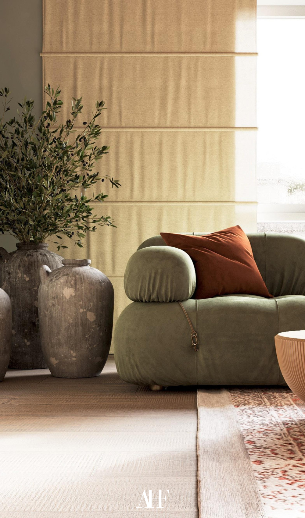 A beautiful living room with a green olive plant to the left of the green sofa. large windows in the background and a statement rug.