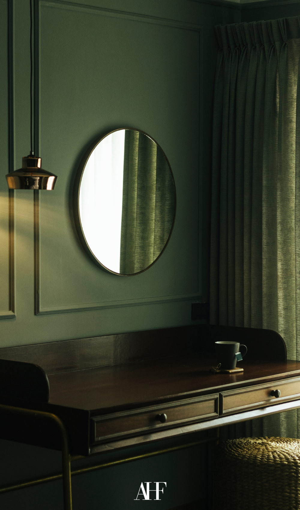 A beautiful green wall with a green console table and a round mirror above it.