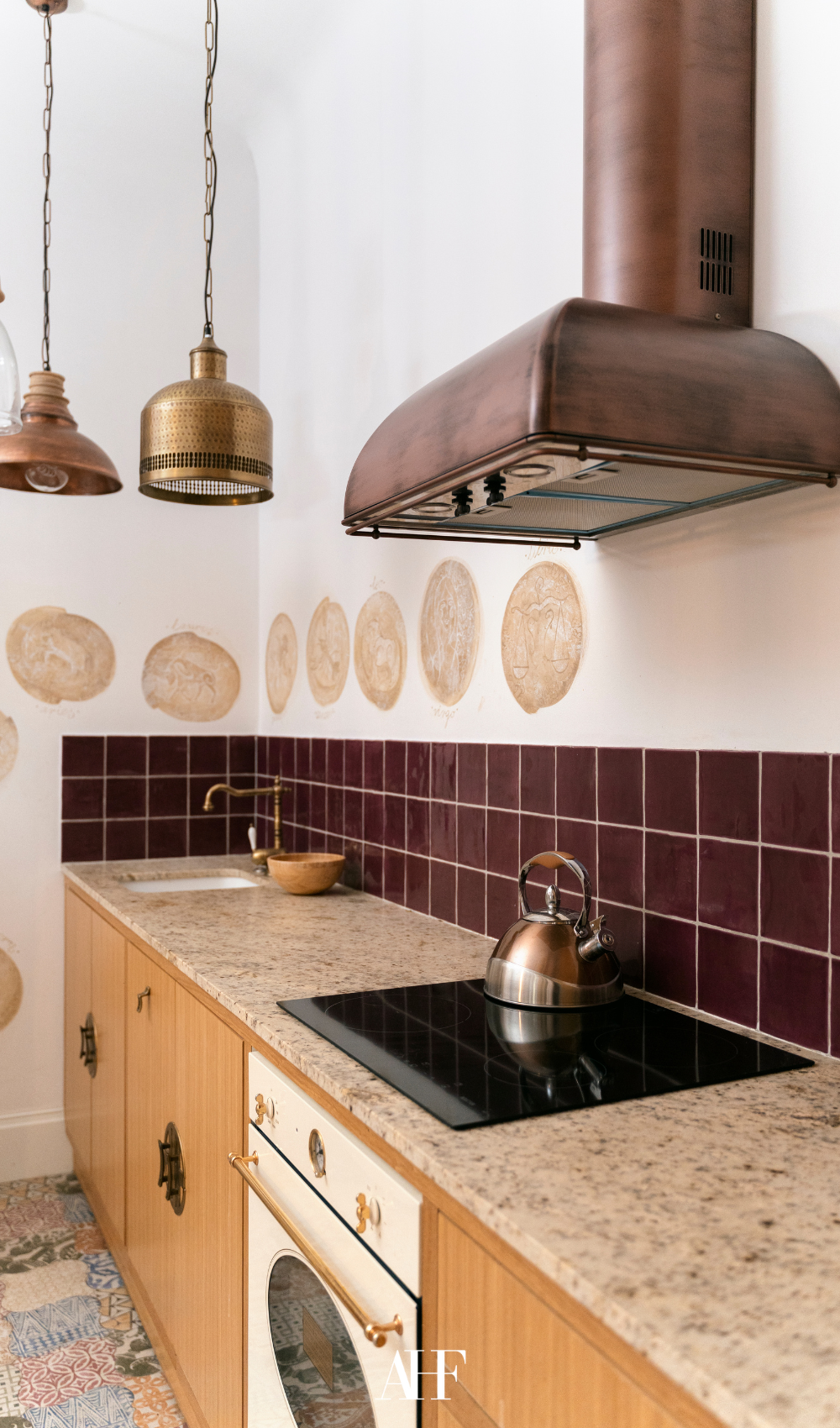 A kitchen with a burgundy backsplash and a rust fan, wooden kitchen cabinets and a stone bench. 
