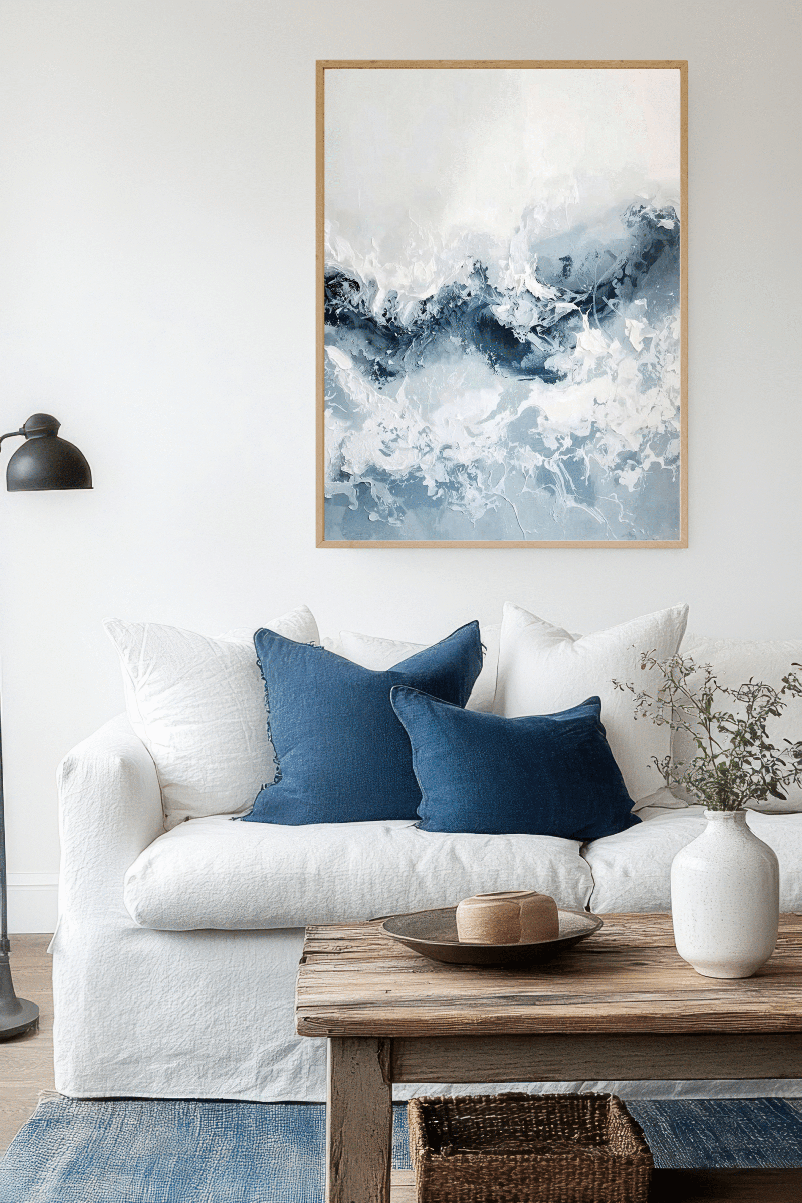 Coastal living room interior with a crisp white sofa and blue pillows, a wooden coffee table and an ocean wall art.