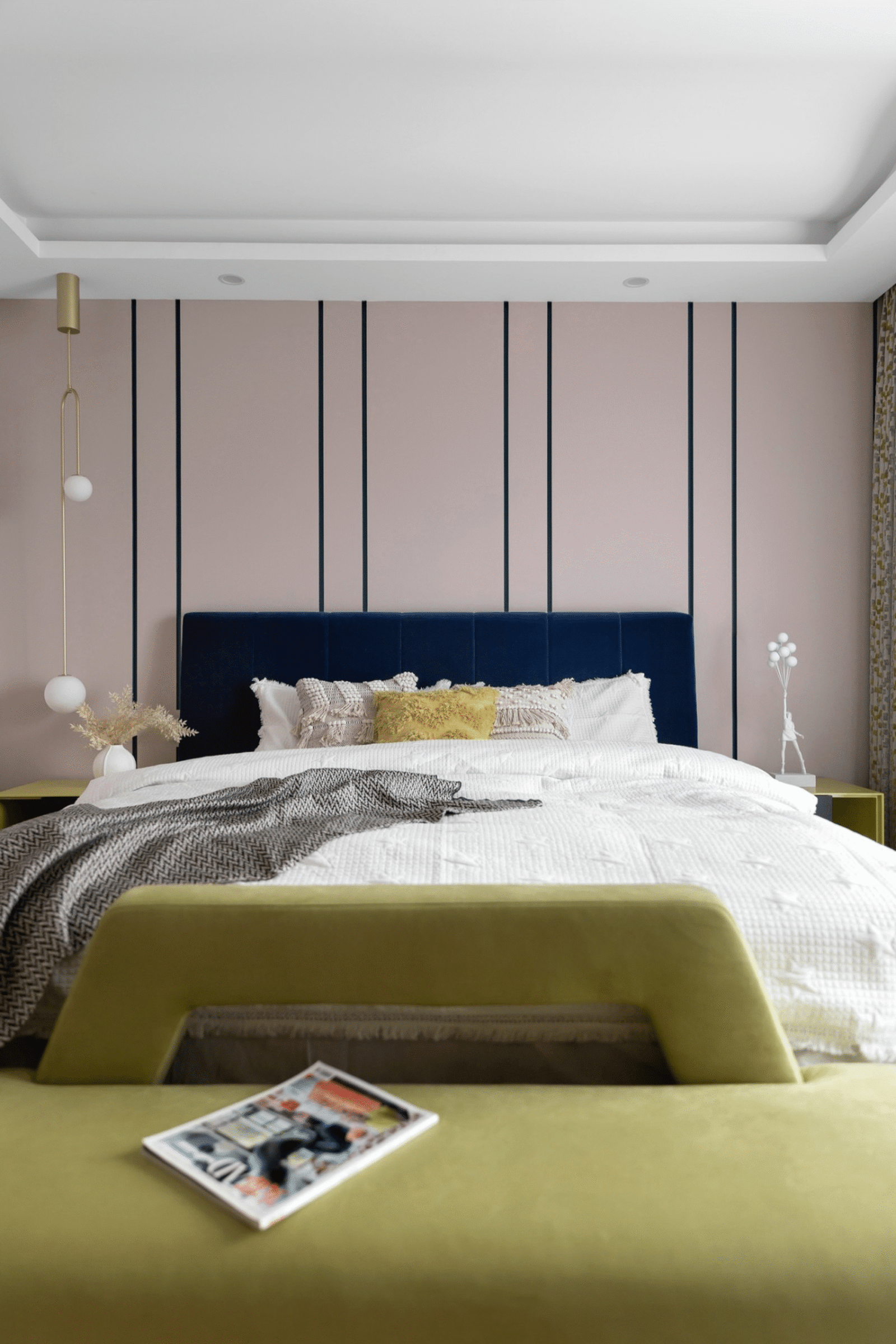 A bedroom with a neutral base and a light green sofa and yellow pillow and a dark blue bed frame.