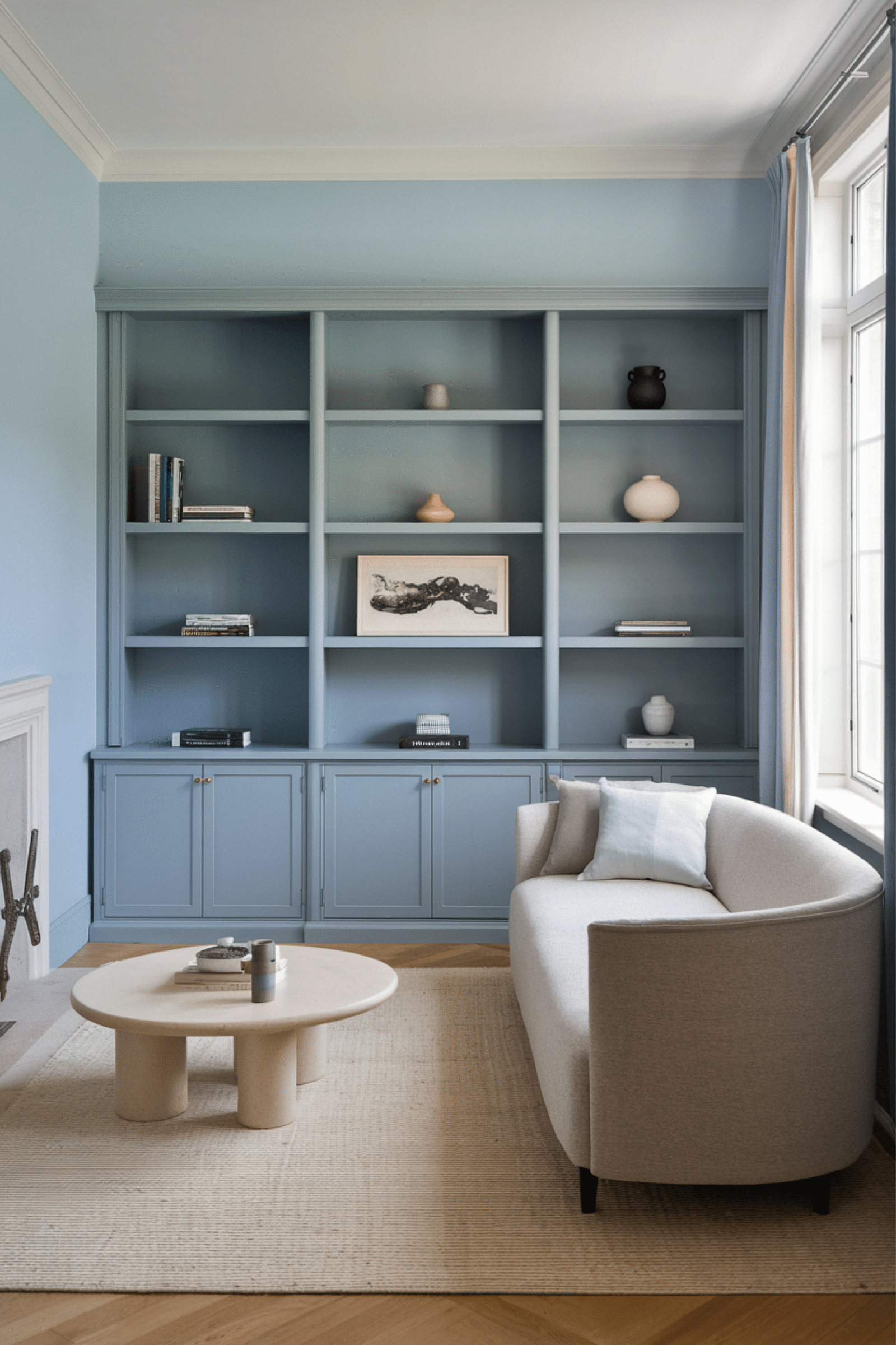 A neutral living room with a light blue book shelf. A neutral coffee table and lots of decor.