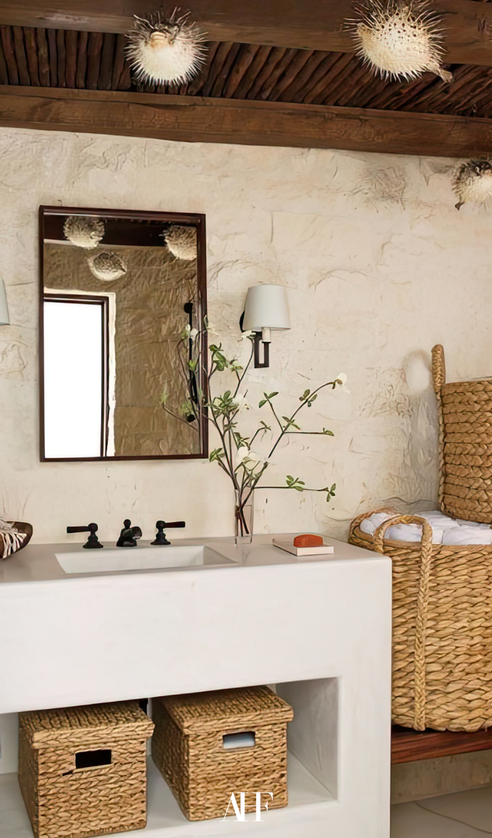 A boho bathroom with a white vanity and baskets with towels in it. A mirror above the sink. 