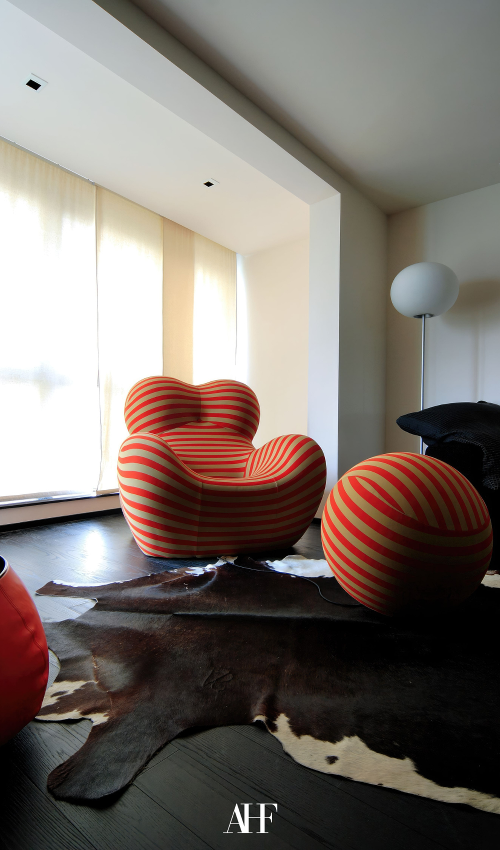 An orange armchair on a black floor with a cow rug . Large windows in the background.
