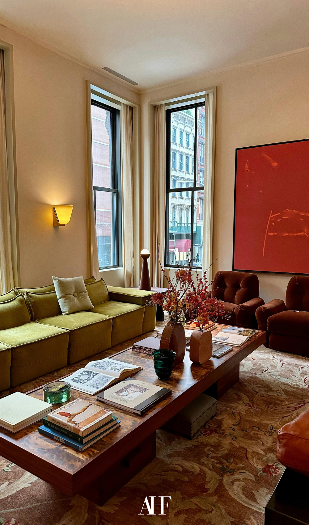 London townhouse style with a green sofa, red wall art and a wooden coffee table. Burgundy armchairs.
