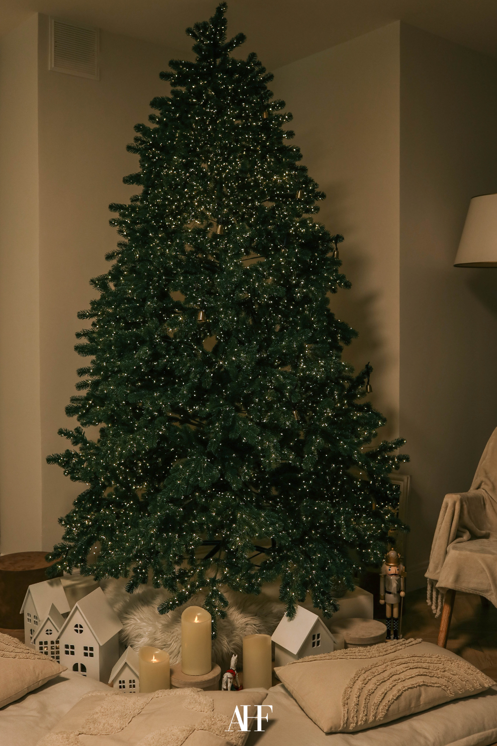A large green Christmas tree with small cute lights in it. A pile of pillows below the tree.